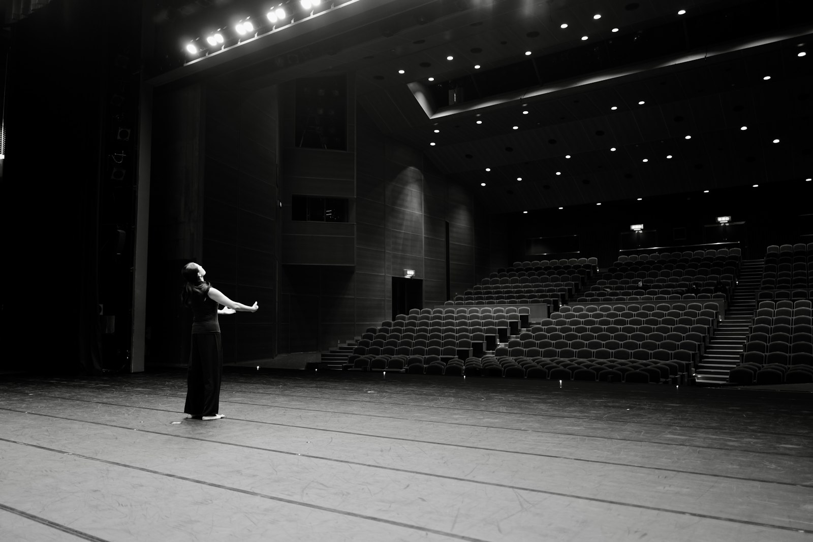 A dancer alone on a stage, arms outstretched towards an empty auditorium